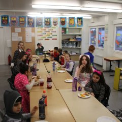 Děti sedí u dlouhého stolu a společně snídají.